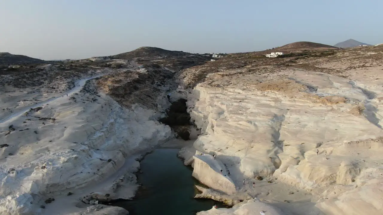 Drone view in Greece flying over a moon shaped white rock area in Milos island at sunrise and the mountain in the horizon