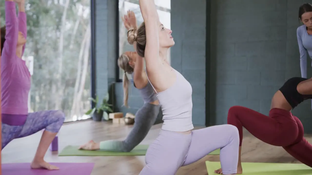 Diverse female instructor assisting women in practicing crescent moon pose in studio