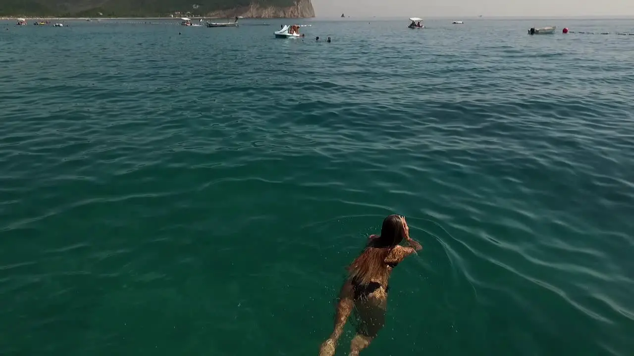 Girl in sea swims areal footage goes up and shows sea water on a summer day