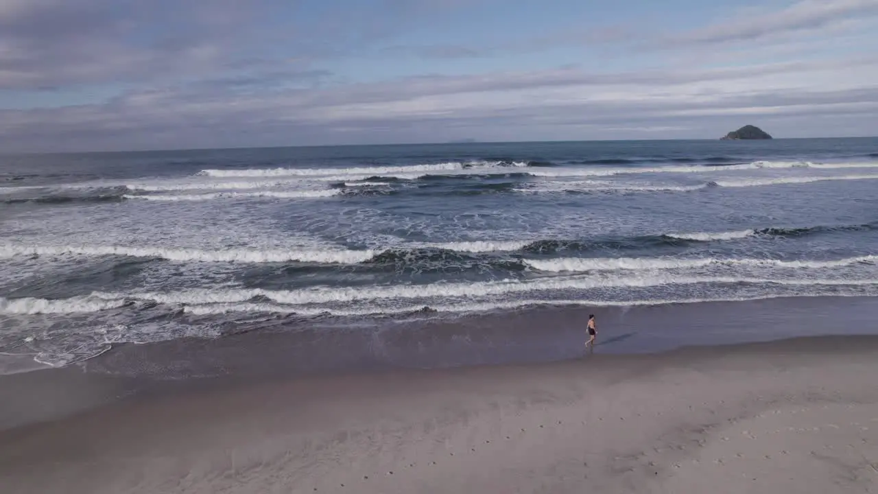 Drone flying up at the shore while a woman walk by the waves