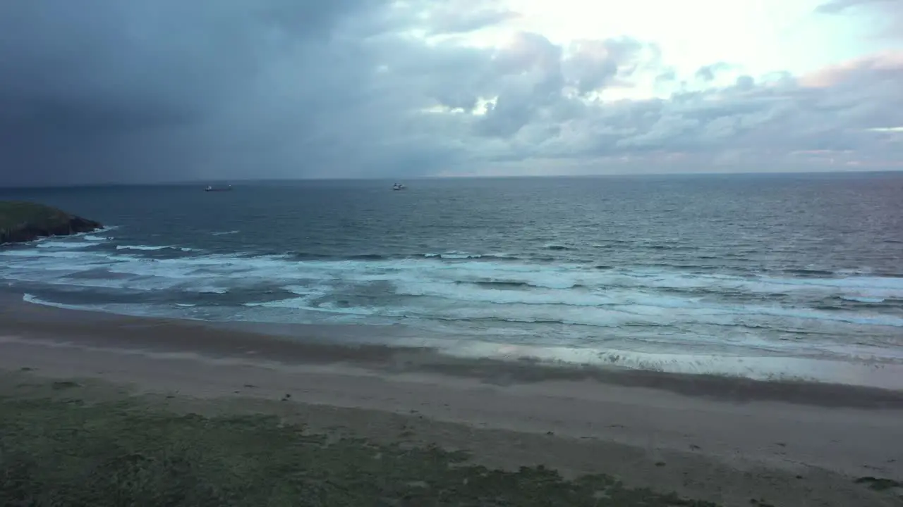 Aerial view of cargo ships on the Atlantic ocean and a beach dark moody evening pan drone shot