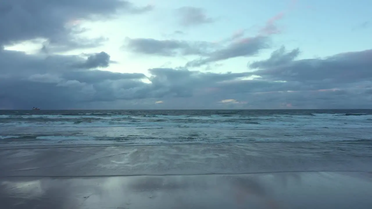 Aerial view over a person stranding on a beach with hands up in air enjoying a gloomy dusk and waves breaking the coast of Spain Dolly drone shot