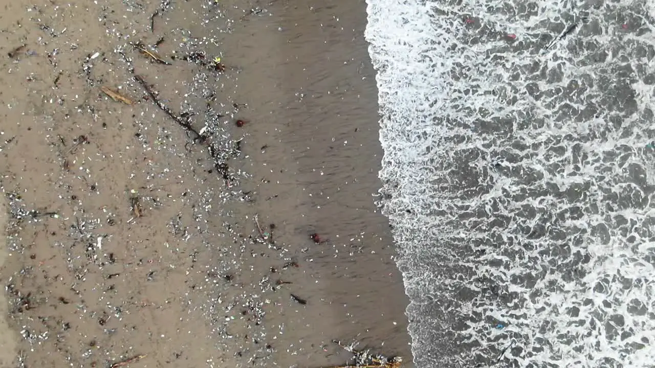 Slow motion aerial shot as waves washing out garbage from the sea polluted ocean coast