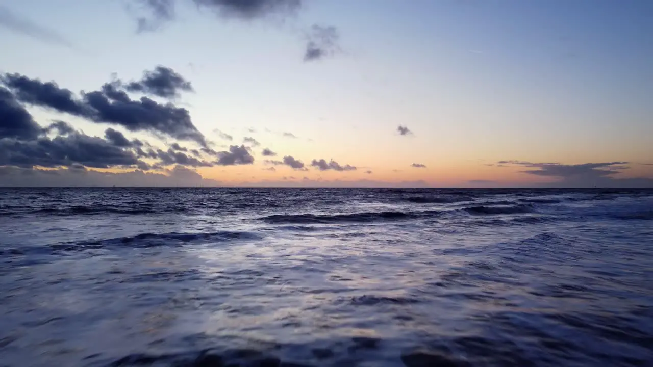 Drone flying fast and low over blue ocean water at beautiful sunset