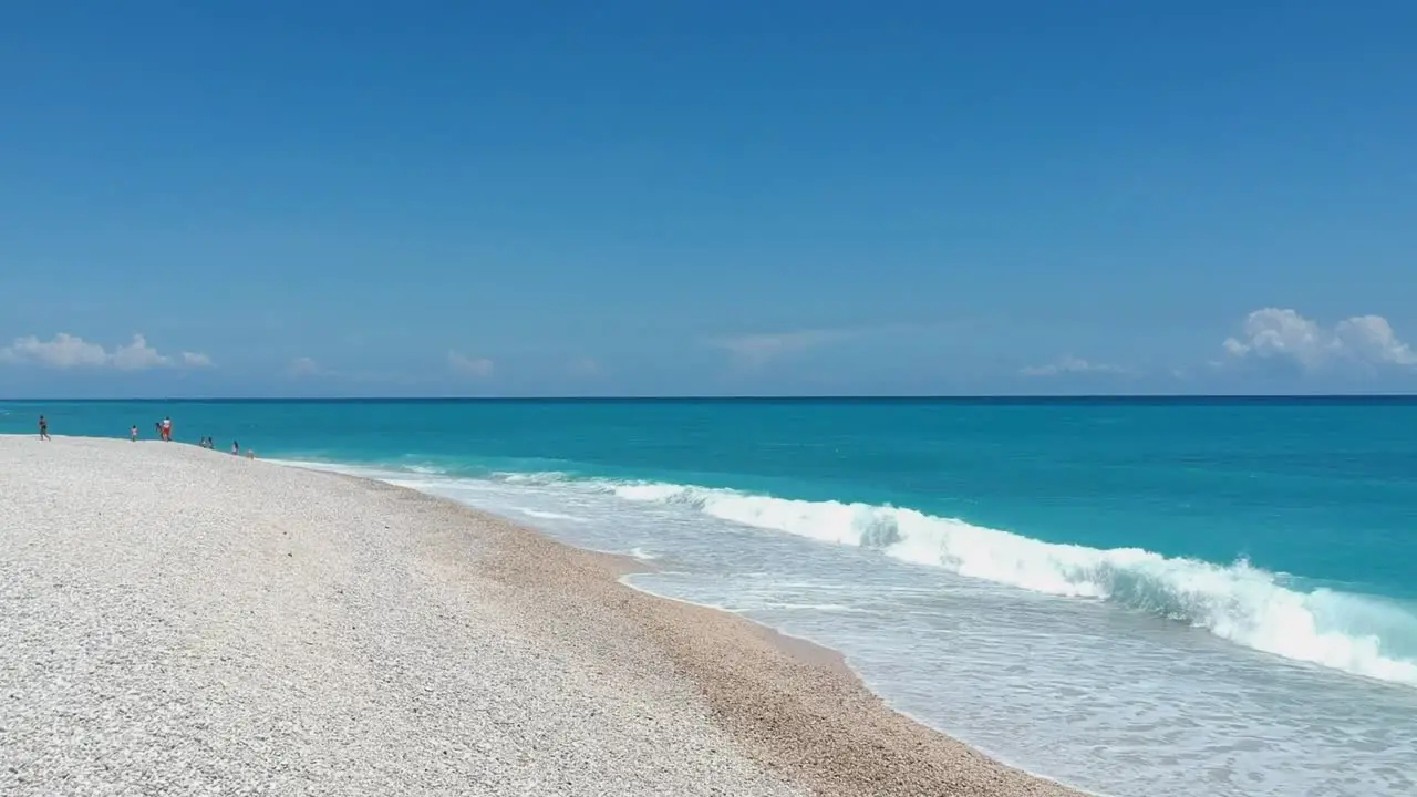 Drone flying low over a white pebble beach toward the blue Caribbean Sea and waves crashing on the shore