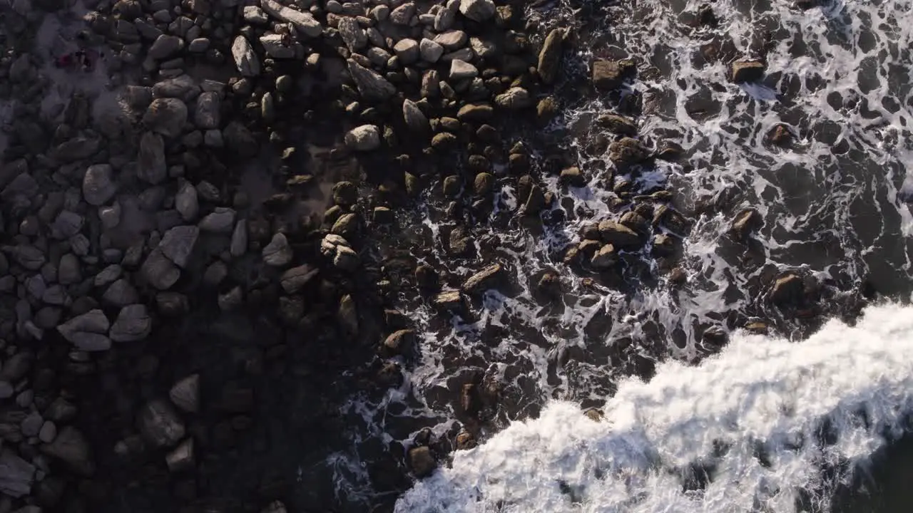 Drone top view moves down closing up waves braking at the beach in the sunlight