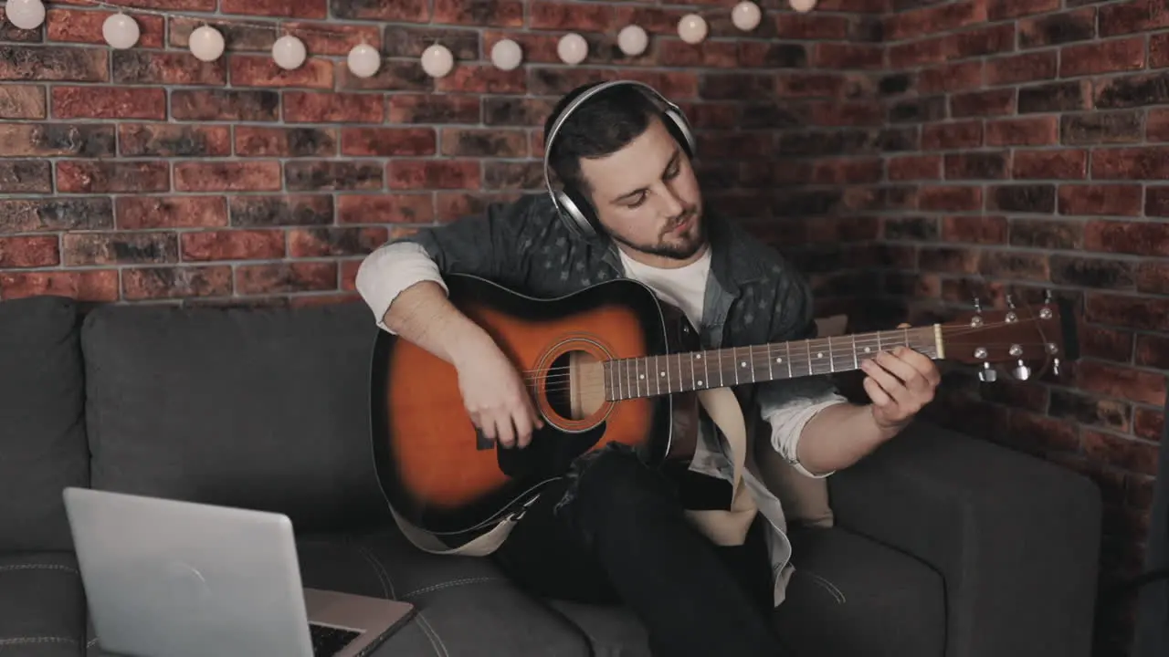 Young Male Musician Playing Guitar And Using Laptop At Home