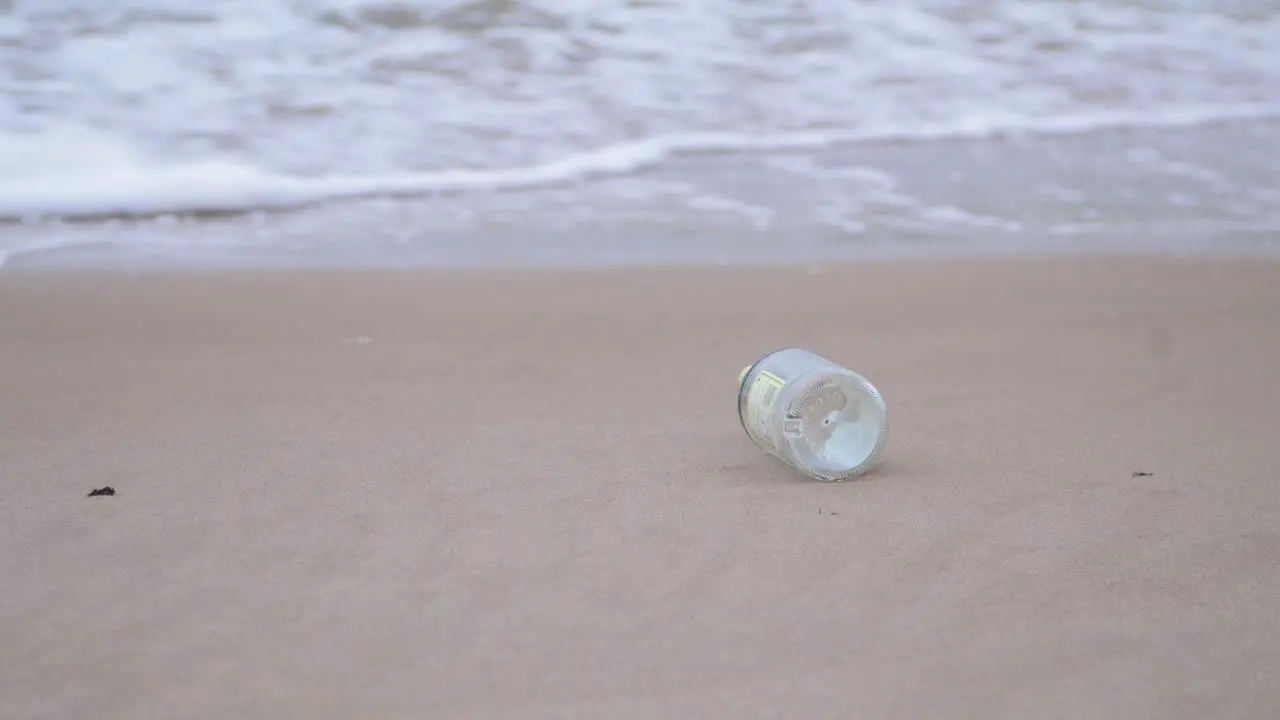 Empty glass bottle on the beach trash and waste litter on an empty Baltic sea white sand beach environmental pollution problem overcast day medium shot