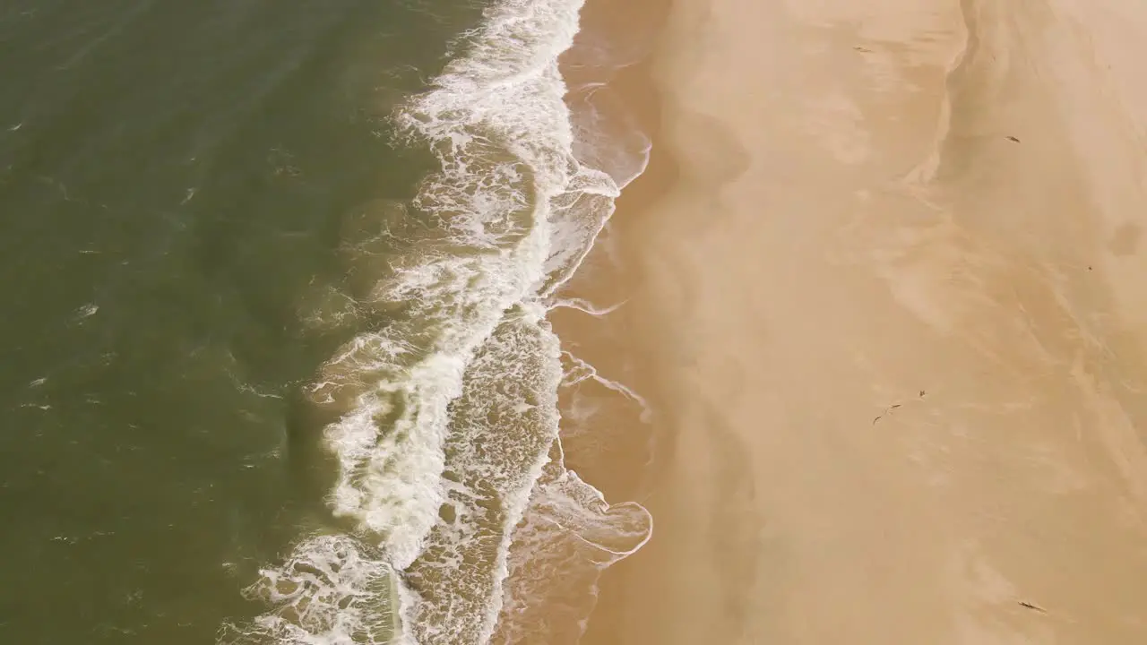 Ocean waves gently crushing into an yellow sand beach drone moving forward over the line formed by the waves and the beach