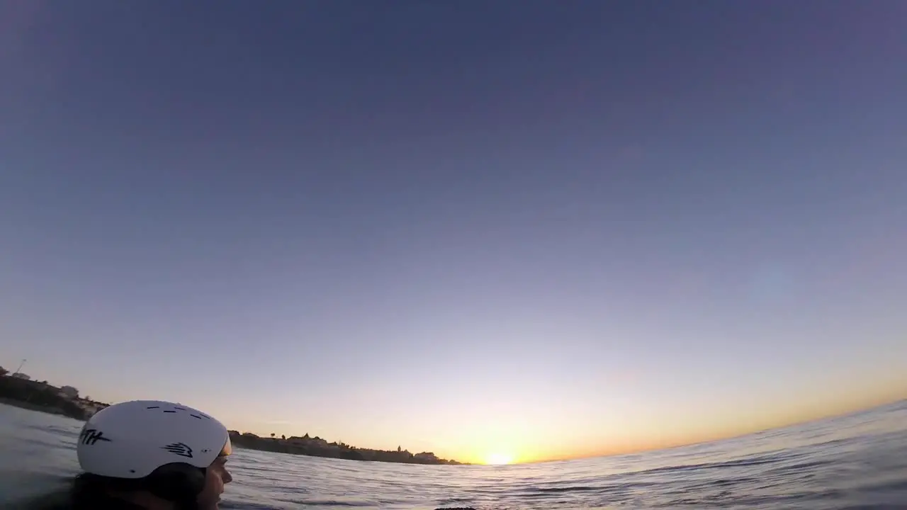 Young causasian man surfer sits on the line up during morning surf session waits his wave and enjoys warm tropical sunrise