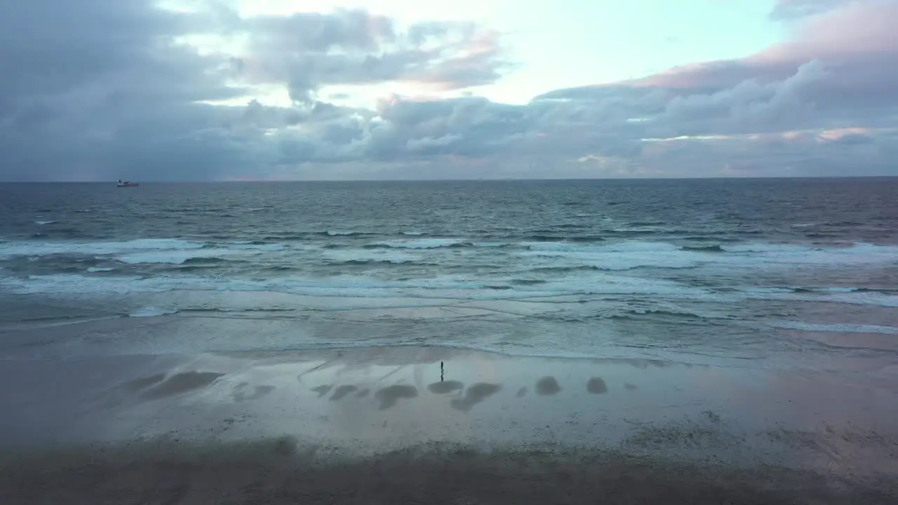 Aerial view of a person walking on a beach dark gloomy evening in Spain Pan drone shot