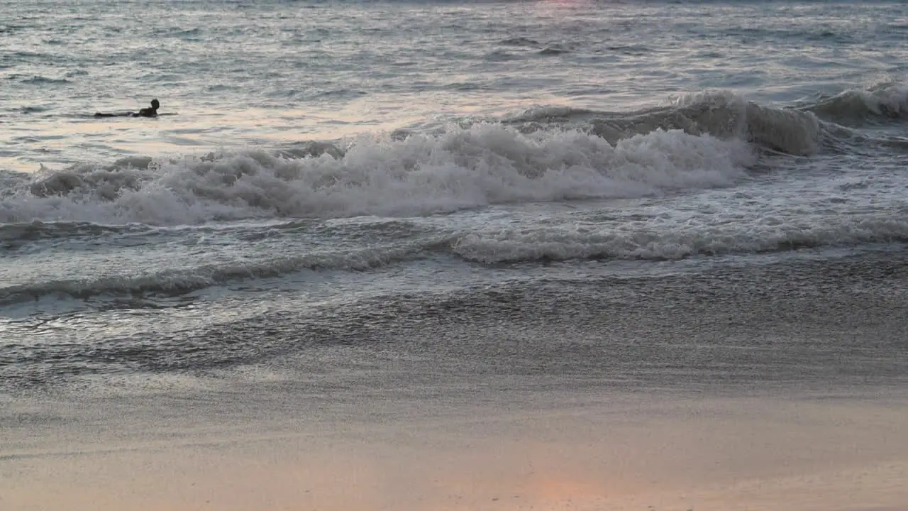 Tilt reveal of surfer paddling in the ocean and a picturesque sunset in the background