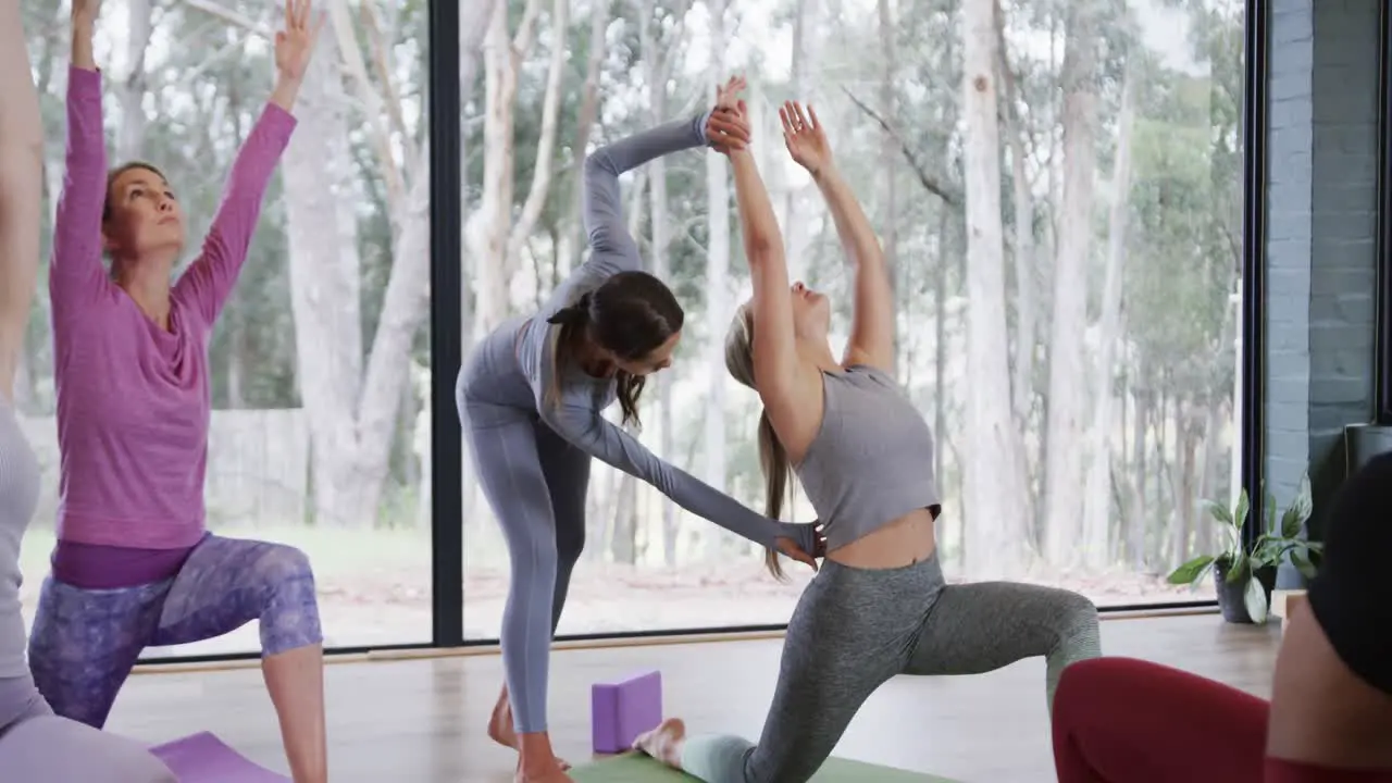 Diverse instructor assisting females in practicing crescent moon pose in yoga studio