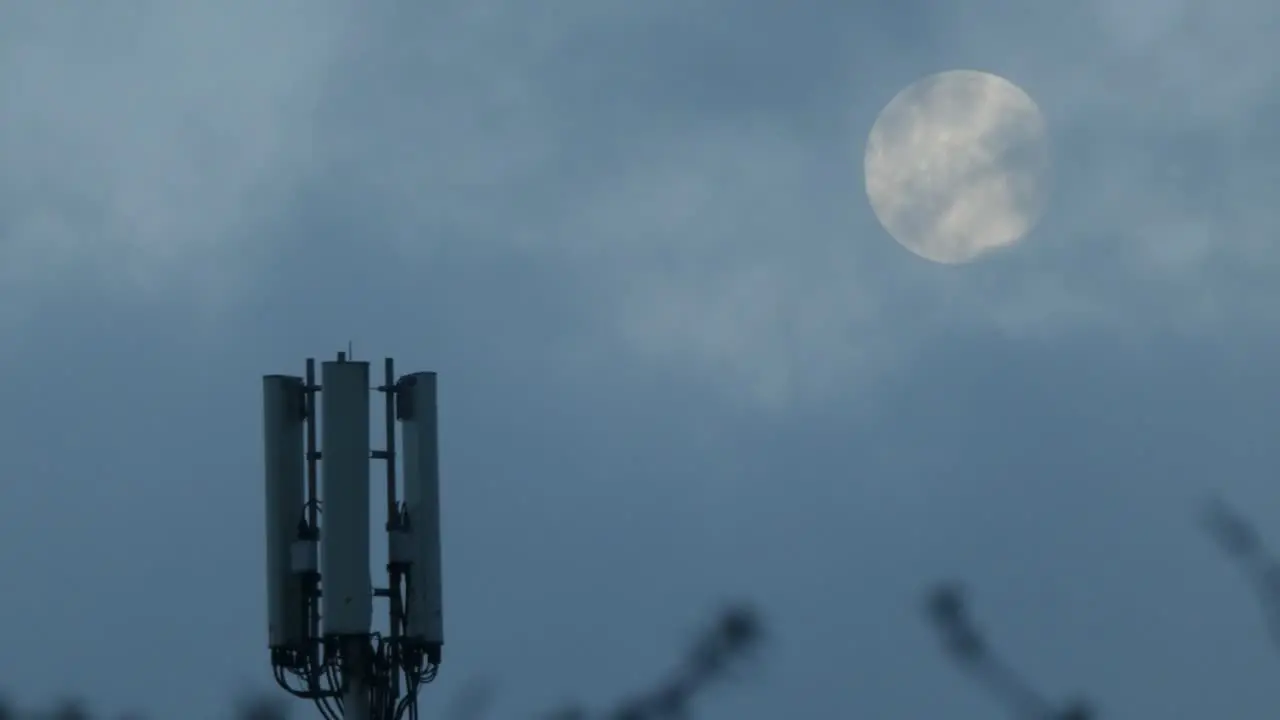 Cloud passing moon behind cellular telecommunication transmission tower antenna