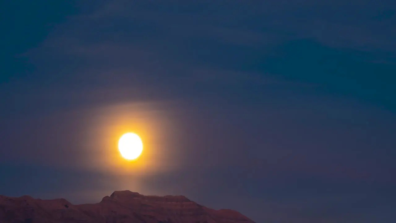 Sunset to nightfall with the glowing full moon rising above the mountain peak time lapse