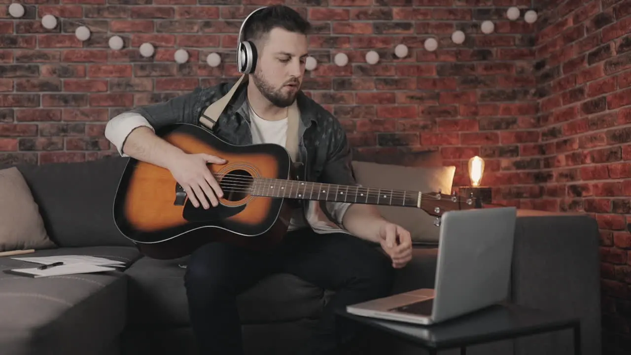 Young Male Musician Creating Playing Guitar And Using Laptop At Home