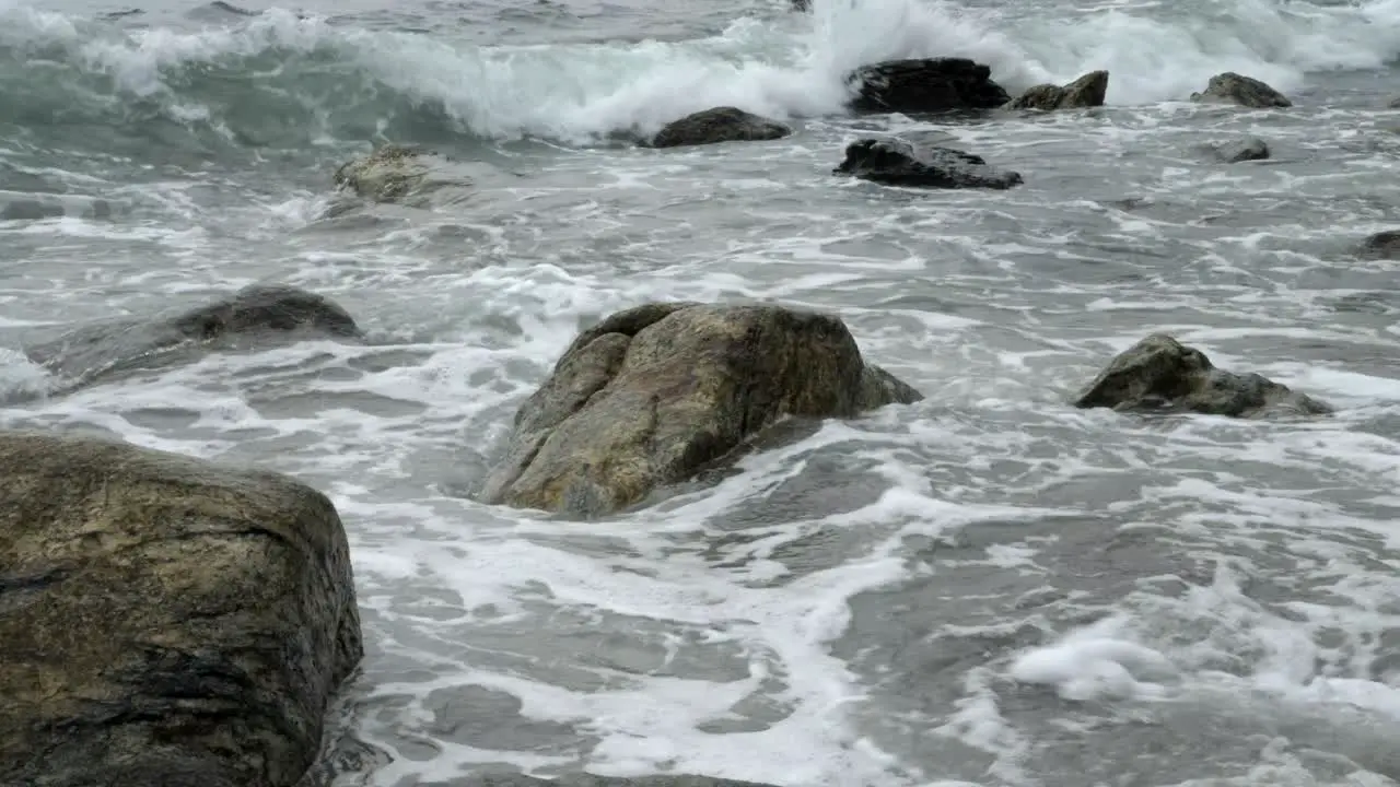 Low angle view across stones poking out from ocean waves on rocky shoreline