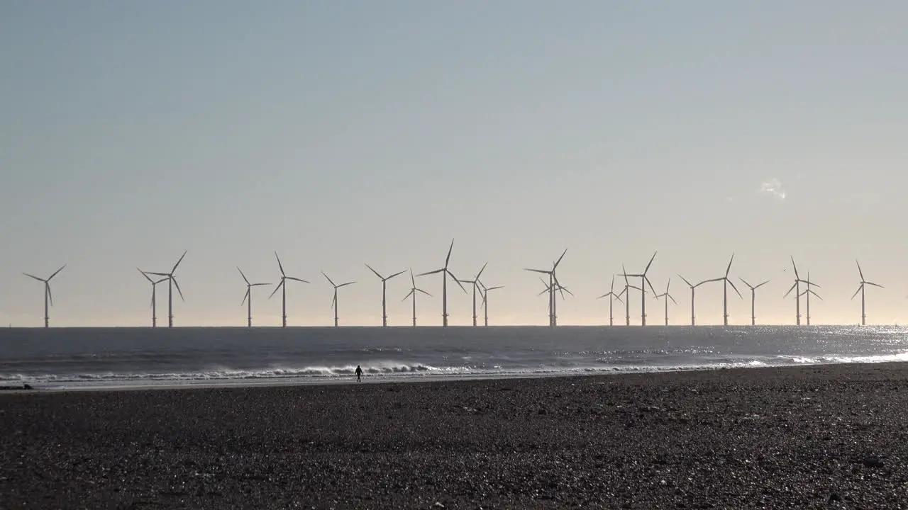 A person walks on beach in front of an offshore wind turbine farm off the coast of Hartlepool in the North Sea