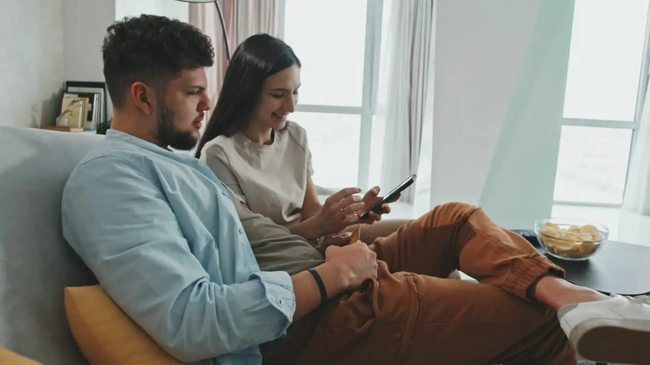 Couple Sitting On The Couch In An Apartment Talking While Using Smartphones