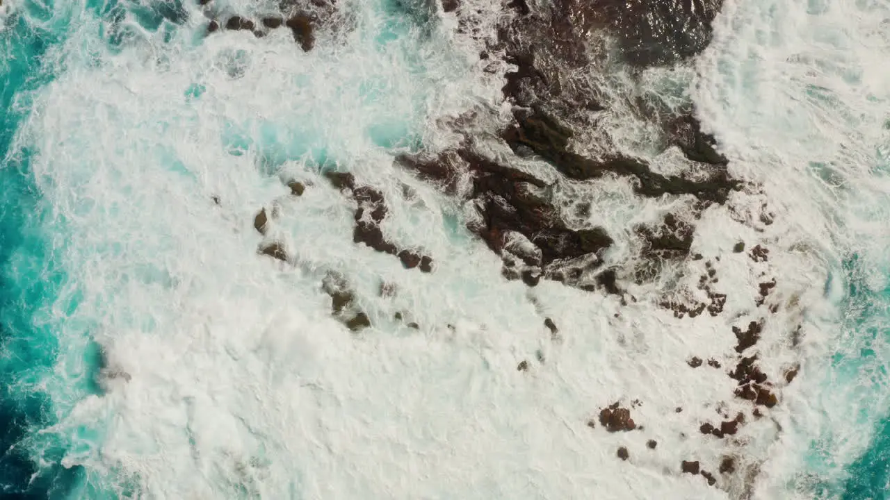 Top down aerial drone shot of waves splashing against the rocks at the shore