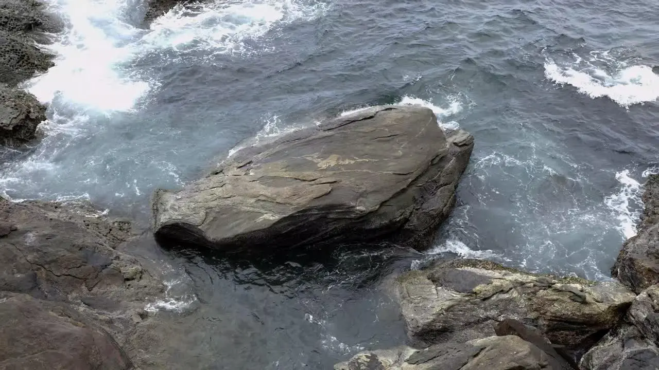 Ocean water moving around large stone on coastal shoreline