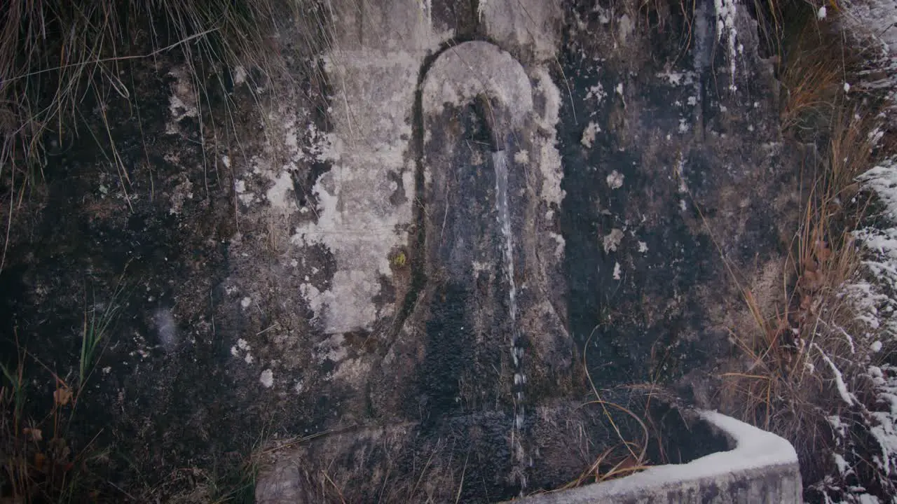 Water flows from vintage water tap in stone wall on winter day