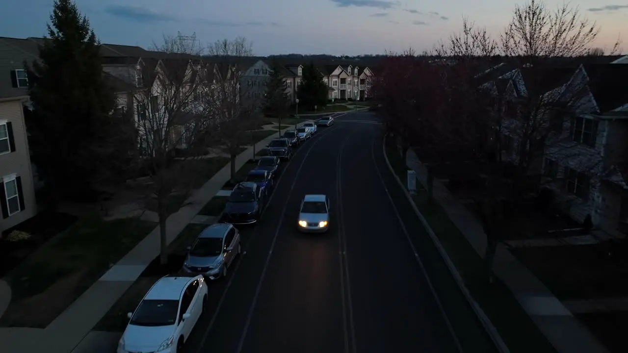 Car drives on street at night past American apartment townhouse homes in evening darkness