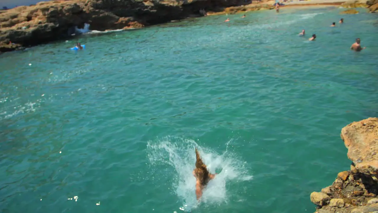 Slow Motion Of A Female Tourist In Swimwear Jumps From The Rocky Edge Into Sea In Summer