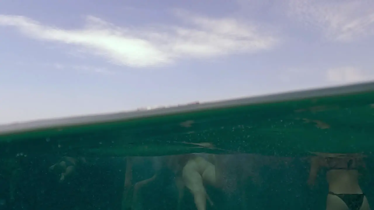 Half underwater sea surface perspective scene of group of girlfriends swimming offshore with dinghy anchored waiting