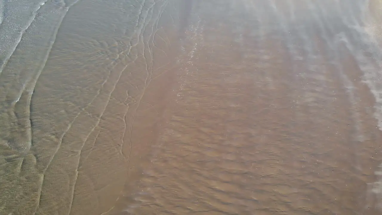 Calm clear ocean waves gently cover sand beach in soft daylight