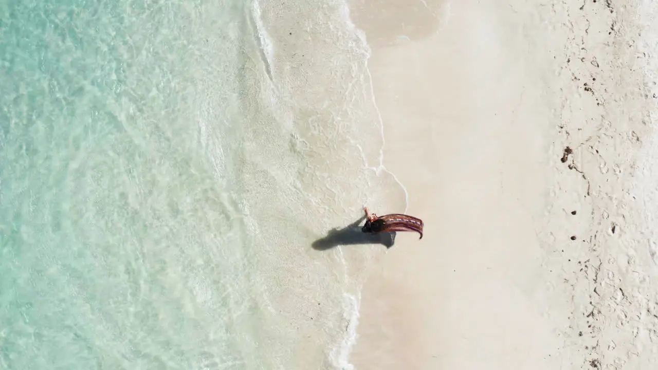 Top down aerial shot of woman walking along idyllic tropical waters and white sand beach Central America