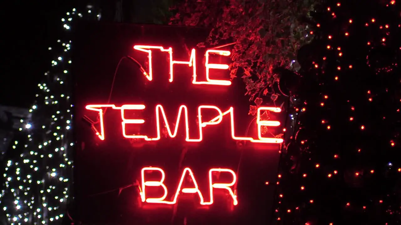 Zooming out shot of a bar singe in red neon lights with some Christmas decorations around it and a Christmas tree