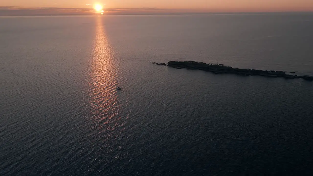 Solitary Sailboat Sailing Through The Sea Near An Island During Sunset aerial shot