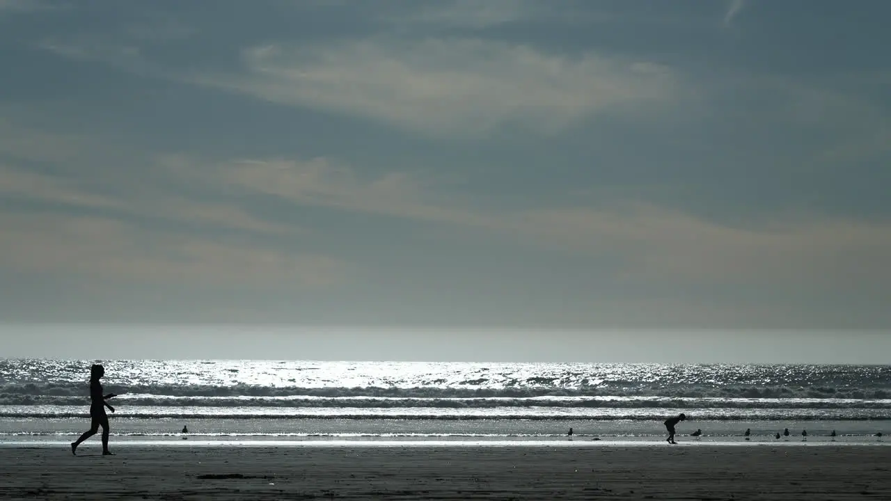 Silhouettes of people on the beach a girl walking and a child searching for seashells in slow motion