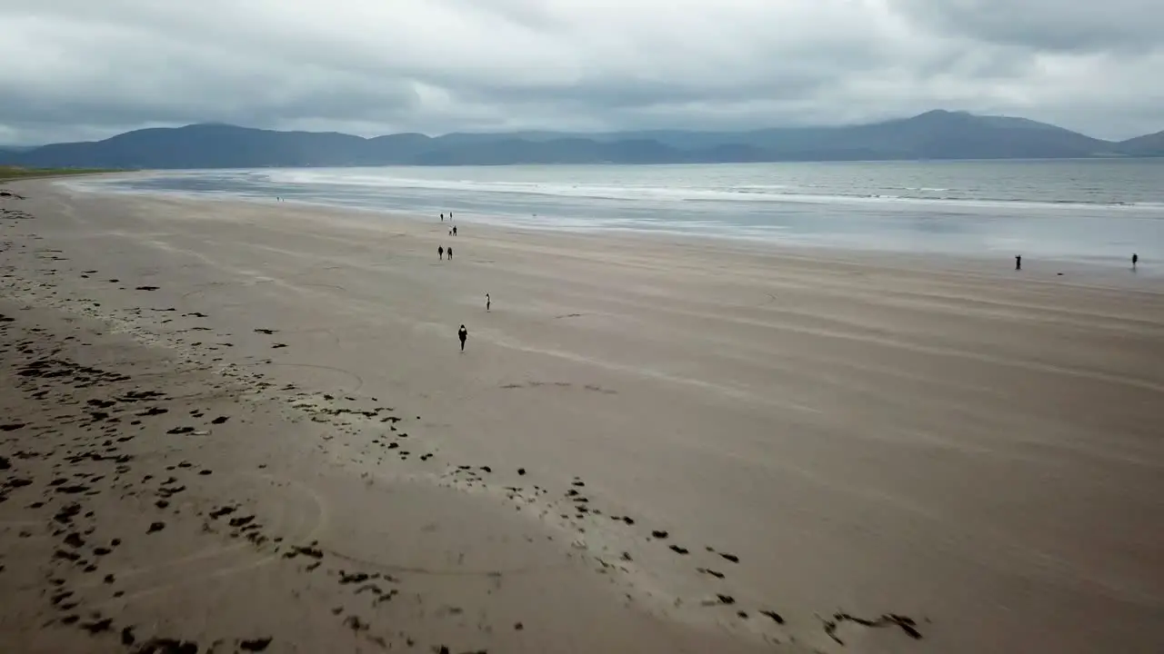 People walk on wide Irish sandy beach Dingle Peninsula