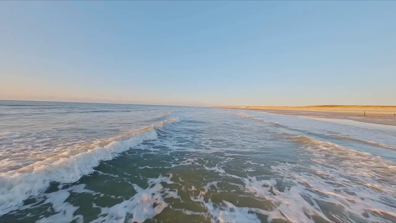 Spectacular FPV drone shot flying closely over breaking waves at high speed during sunset on a cloudless day