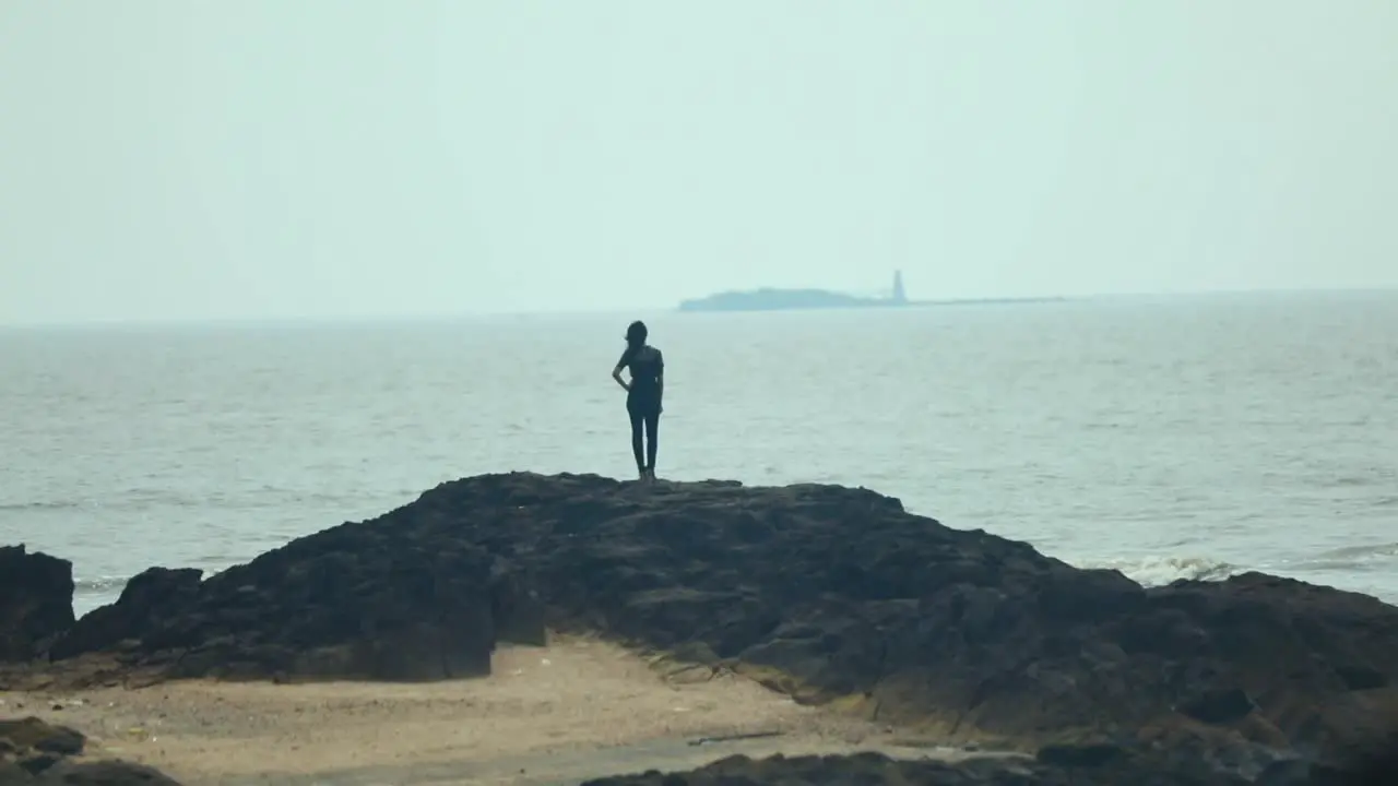 girl standing on rock moving sea waves in back long shot