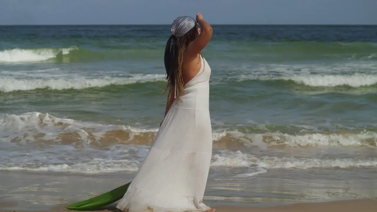 Young girl in a beach dress walks on the beach with ocean waves in the background