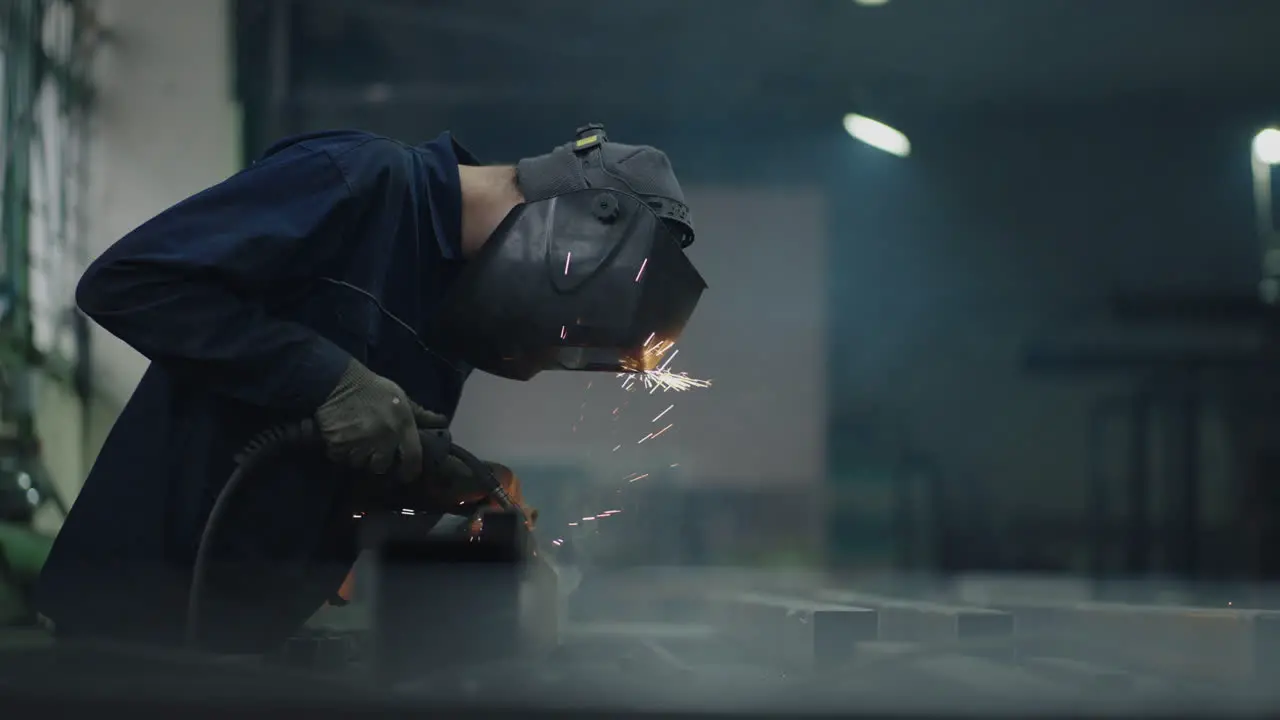 Portrait A man welder works in a factory and welds steel metal parts in slow motion Sparks fly