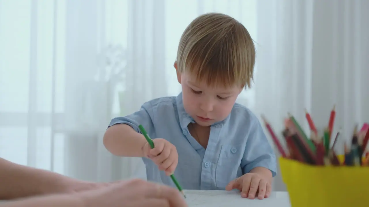 The boy draws a pencil picture of a happy family sitting at the table