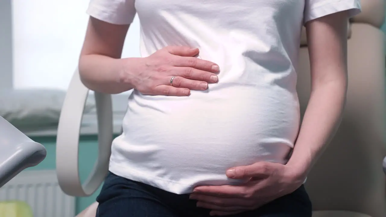 Camera Focuses On Pregnant Woman's Hands Touching Her Belly In The Medical Consultation 1