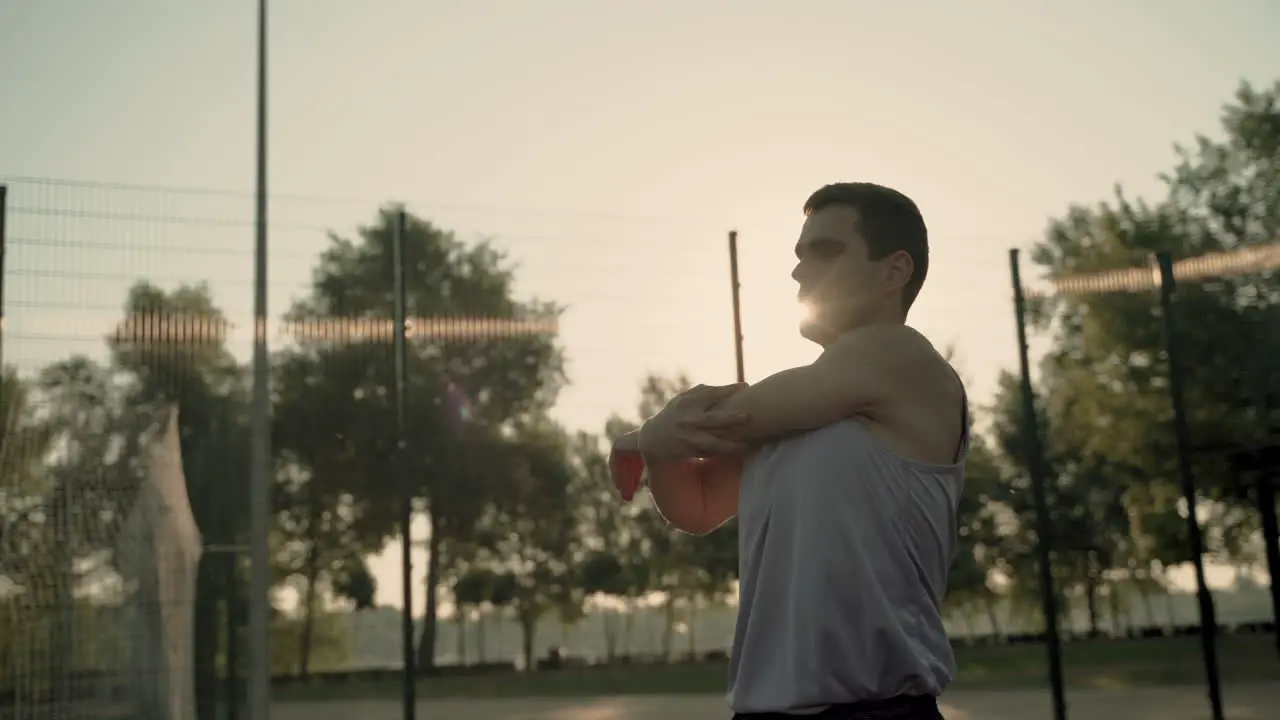 Concentrated Sportsman Doing Deltoid And Tricep Stretch Exercises In Outdoor Court At Sunset