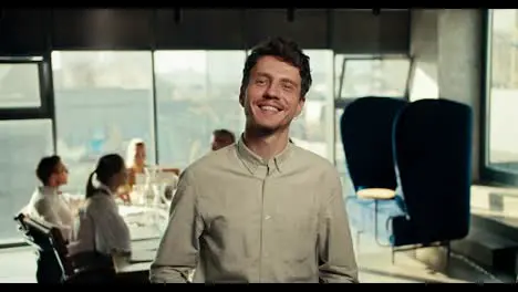 Happy guy office worker in a white shirt posing in the office against the background of his colleagues