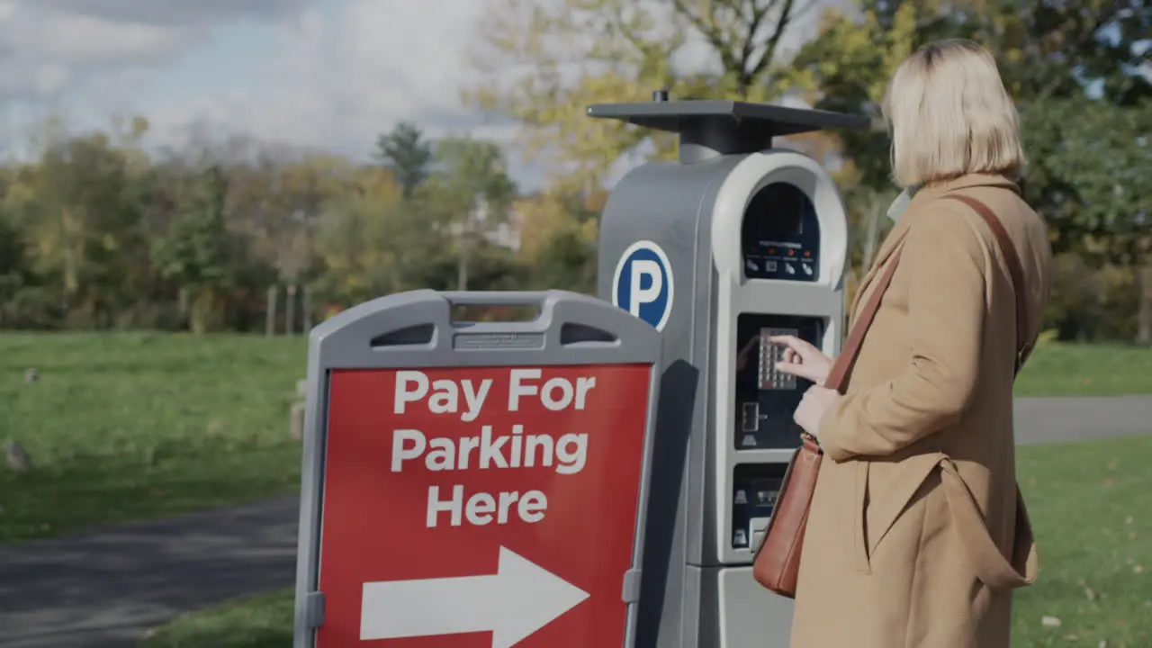 A woman pays for parking a car uses a solar-powered parking meter