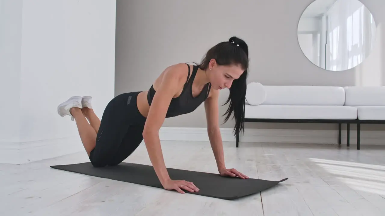 Young sexy brunette woman in sportswear performs pushups kneeling at home on a rug