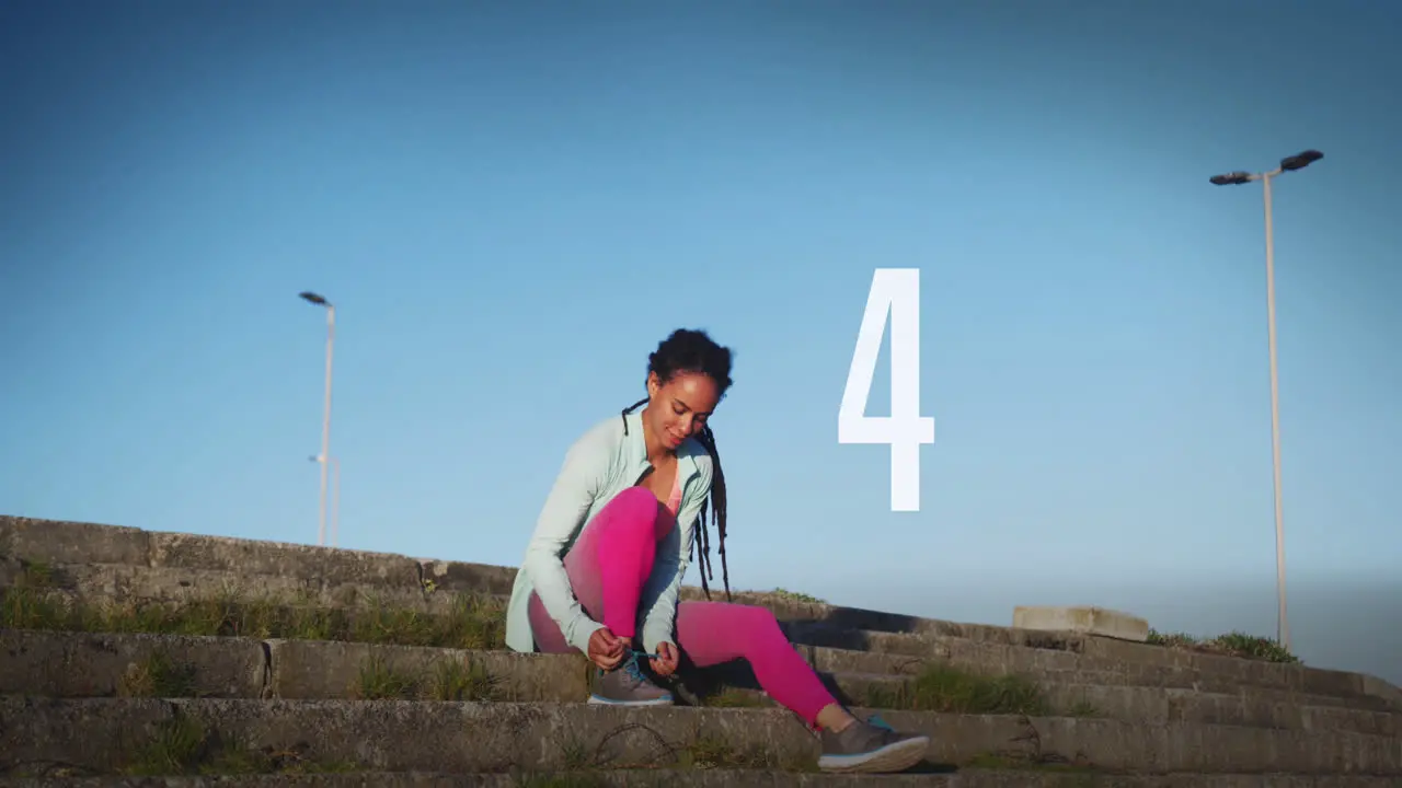 Number countdown against african american fit woman tying her shoe laces sitting on the stairs