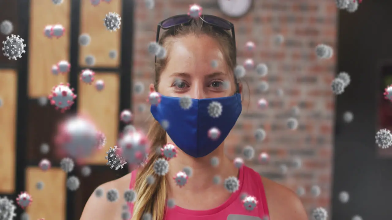 Multiple covid-19 cells floating against portrait of caucasian fit woman wearing a mask at the gym