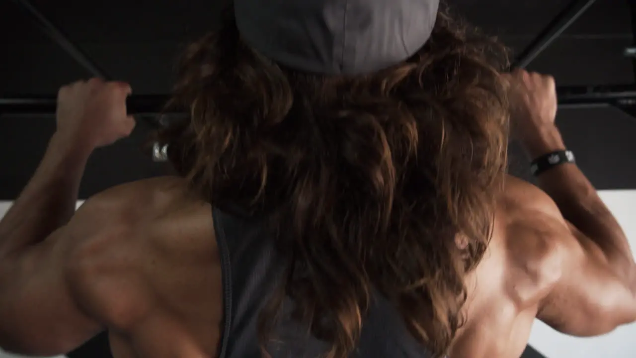 Muscular man with long hair doing pull ups in a dark gym and showing his back muscles