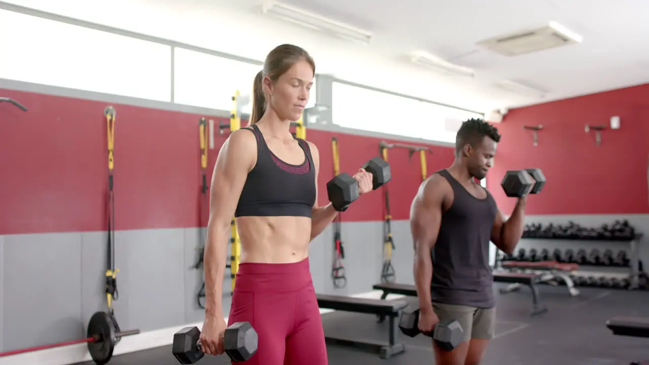 Fit young Caucasian woman and African American man lifting weights at the gym