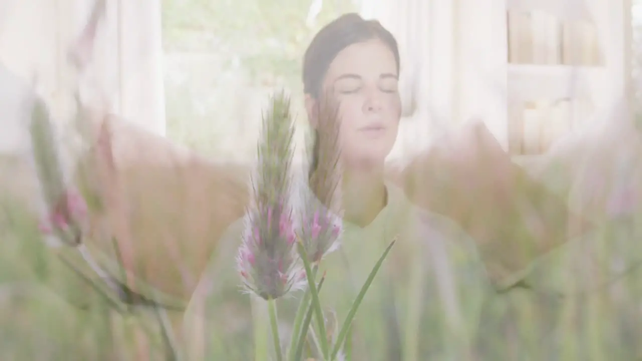 Animation of meadow over woman exercising and meditating at home